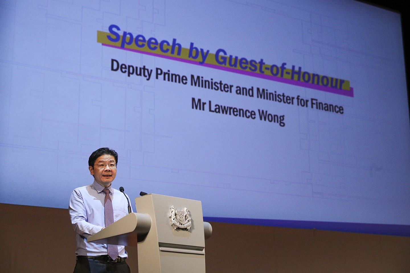 Lawrence Wong speaks at a podium, screen reads: "Speech by Guest-of-Honour".